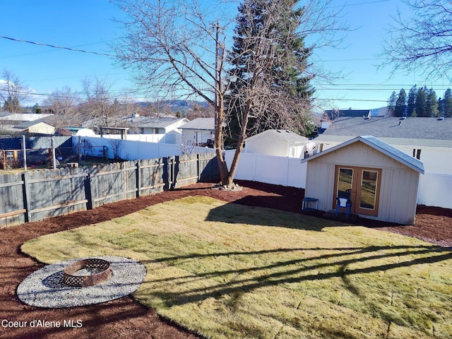 view of yard with an outbuilding, french doors, a fenced backyard, and a fire pit