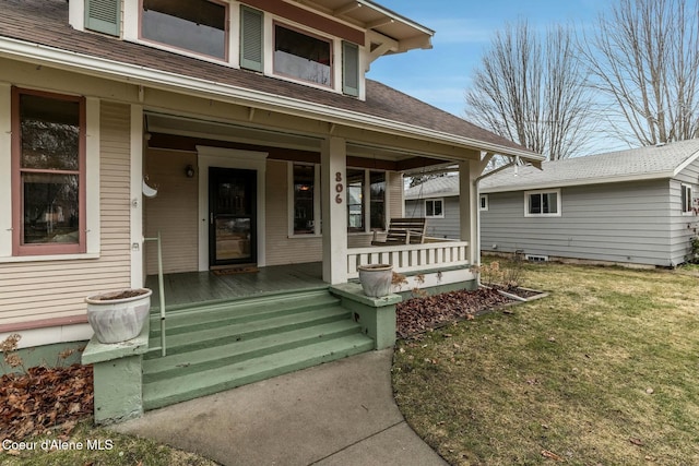 entrance to property featuring covered porch, roof with shingles, and a lawn