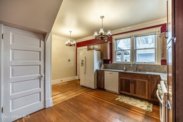 kitchen with a notable chandelier, white appliances, a sink, ornamental molding, and hardwood / wood-style floors