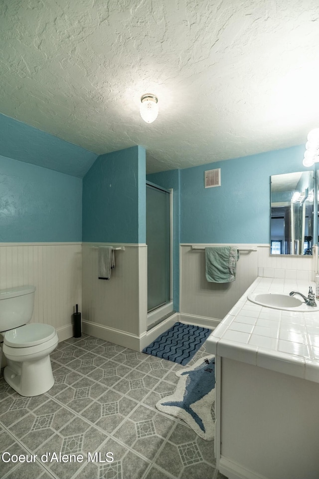 full bath with a wainscoted wall, visible vents, toilet, a stall shower, and a textured ceiling