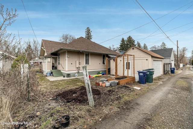 view of side of property with an outbuilding, a shingled roof, fence, a garden, and driveway