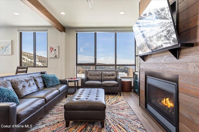 living area featuring wood finished floors, a glass covered fireplace, beam ceiling, and a healthy amount of sunlight