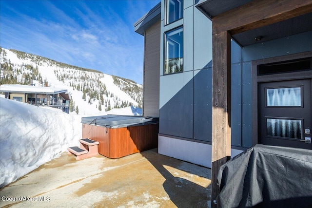 view of snow covered exterior featuring a patio area, a mountain view, and a hot tub