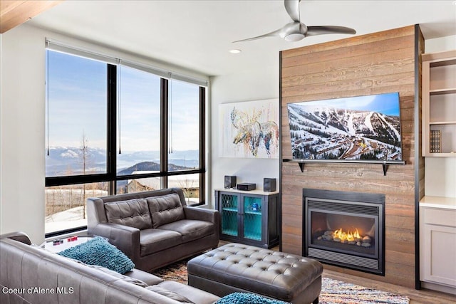 living area featuring a large fireplace, ceiling fan, expansive windows, and wood finished floors