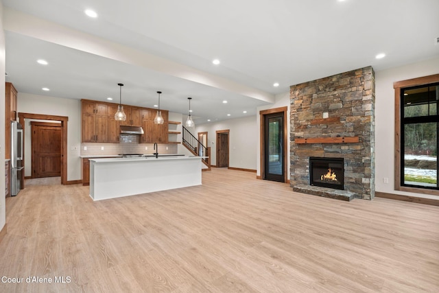 kitchen featuring under cabinet range hood, open floor plan, backsplash, freestanding refrigerator, and light wood finished floors