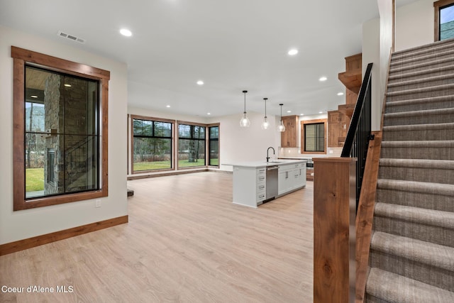 kitchen with visible vents, open floor plan, light countertops, light wood-type flooring, and an island with sink