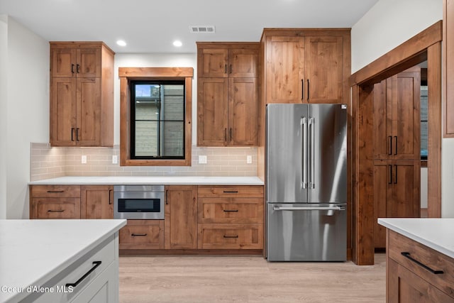 kitchen with appliances with stainless steel finishes, light wood-type flooring, visible vents, and backsplash