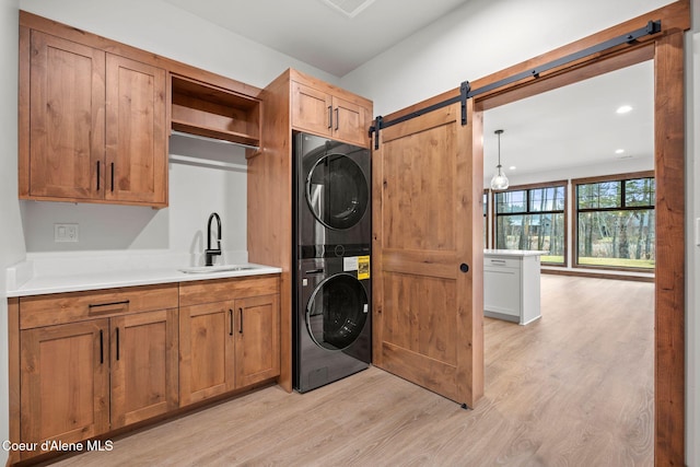 washroom with cabinet space, a barn door, light wood-style floors, stacked washer / dryer, and a sink