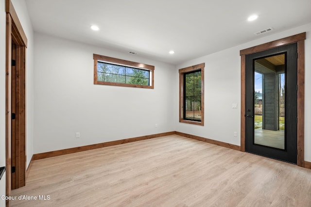 empty room with light wood finished floors, visible vents, and baseboards