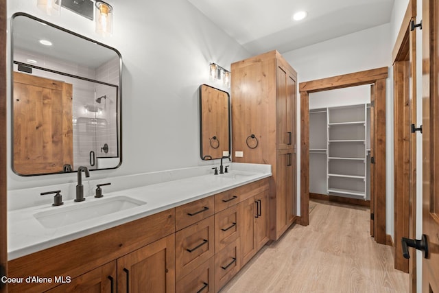 full bath featuring a stall shower, wood finished floors, a sink, and double vanity