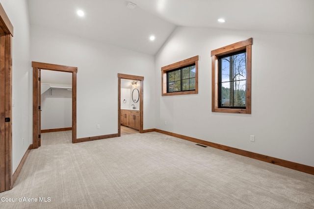 unfurnished bedroom featuring baseboards, visible vents, light colored carpet, vaulted ceiling, and a walk in closet