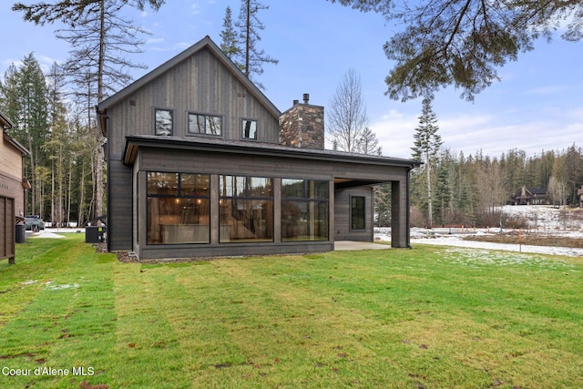 rear view of property with a sunroom, a chimney, and a lawn