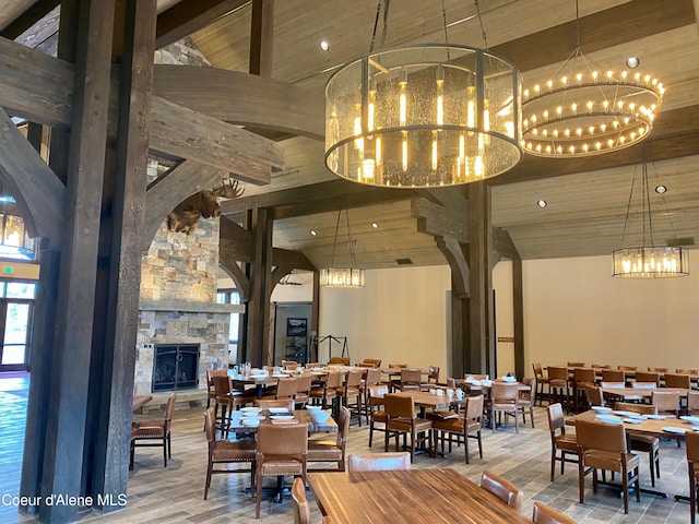 dining area with beam ceiling, an inviting chandelier, a stone fireplace, high vaulted ceiling, and wooden ceiling