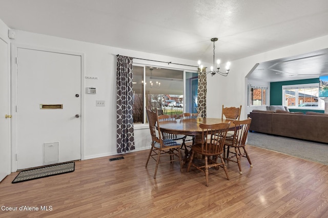 dining space with arched walkways, visible vents, wood finished floors, a chandelier, and baseboards