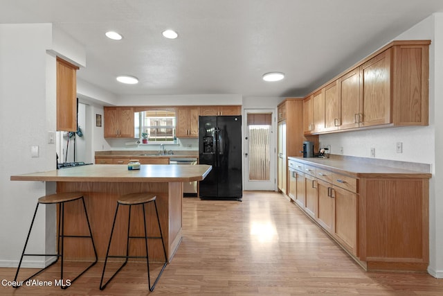 kitchen with a peninsula, a kitchen breakfast bar, light wood-style floors, black fridge, and dishwasher