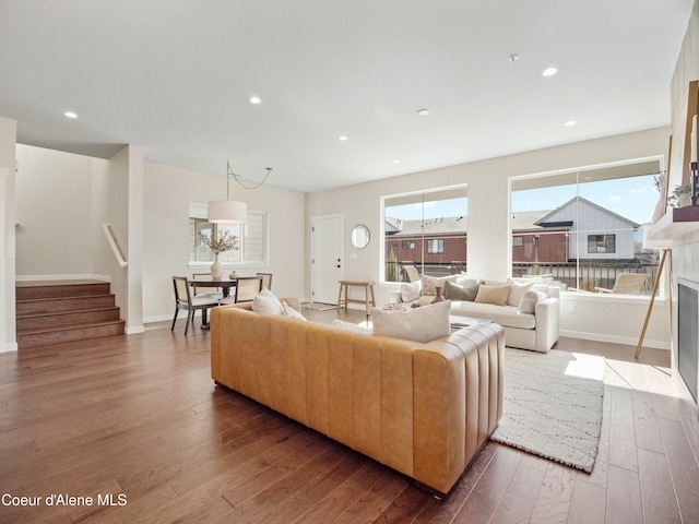 living area featuring a fireplace with flush hearth, wood finished floors, recessed lighting, stairway, and baseboards