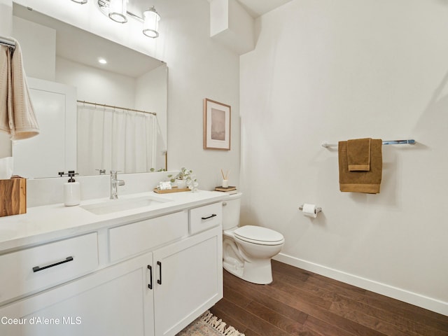 bathroom with vanity, toilet, wood finished floors, and baseboards