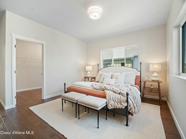 bedroom with dark wood-style floors, a closet, a walk in closet, and baseboards