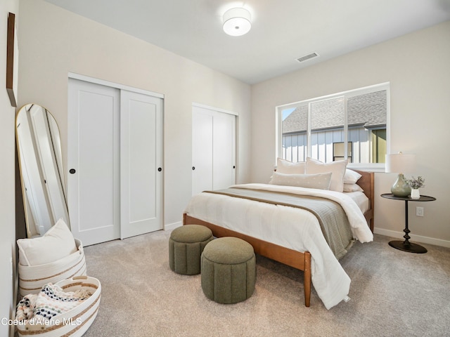 carpeted bedroom featuring visible vents, baseboards, and multiple closets