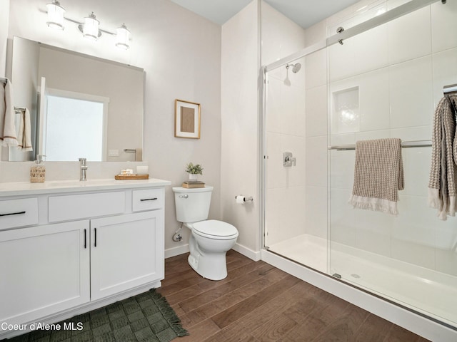 full bathroom with a shower stall, baseboards, toilet, wood finished floors, and vanity