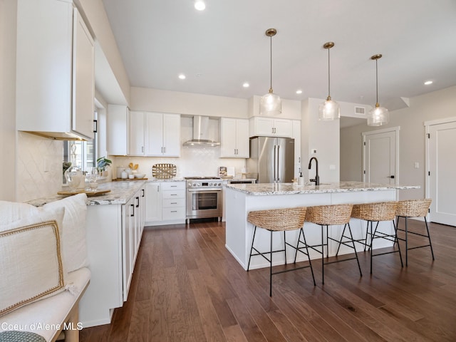 kitchen featuring wall chimney range hood, a breakfast bar area, white cabinets, stainless steel appliances, and dark wood-style flooring