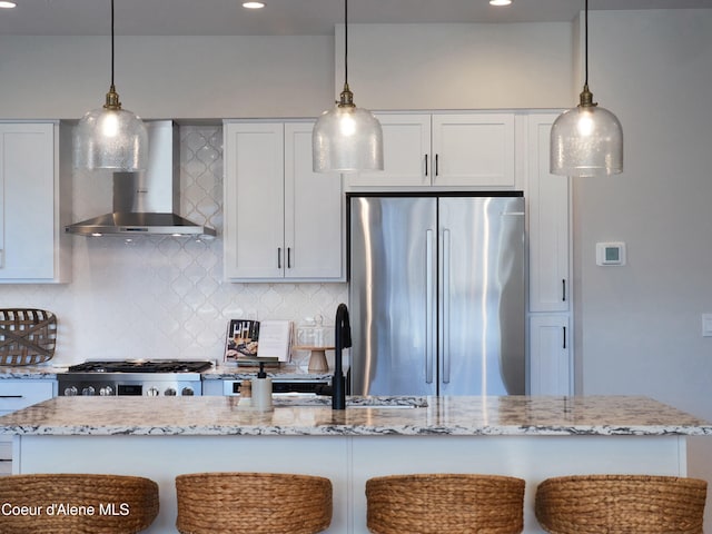 kitchen featuring light stone counters, freestanding refrigerator, wall chimney range hood, range, and backsplash