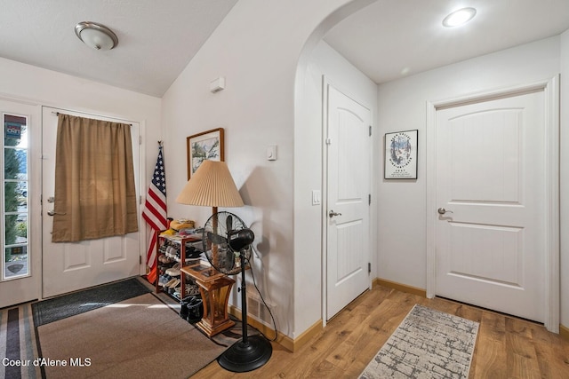 foyer entrance featuring baseboards, arched walkways, wood finished floors, and vaulted ceiling