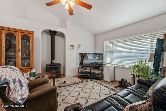 living area with wood finished floors, a ceiling fan, a wood stove, arched walkways, and vaulted ceiling