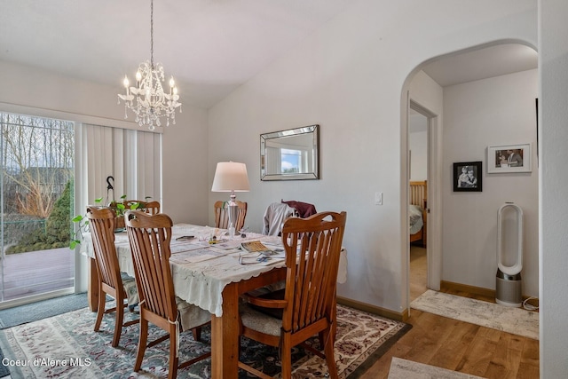 dining space featuring baseboards, vaulted ceiling, wood finished floors, arched walkways, and a notable chandelier