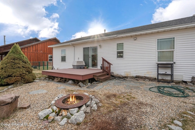 back of property with a shingled roof, a fire pit, a deck, and fence