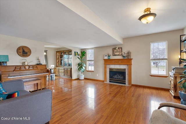 living room featuring a tiled fireplace, wood finished floors, a wealth of natural light, and baseboards