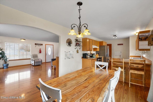 dining area with light wood-type flooring, arched walkways, and a chandelier