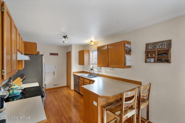 kitchen featuring brown cabinets, appliances with stainless steel finishes, a sink, a peninsula, and under cabinet range hood