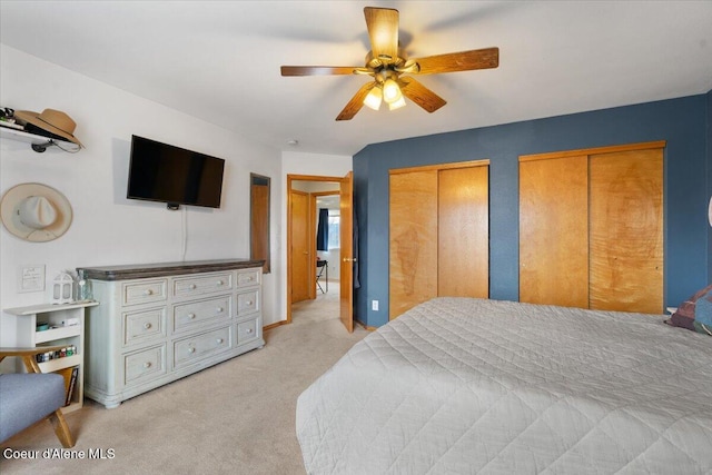 bedroom featuring light carpet, a ceiling fan, and multiple closets