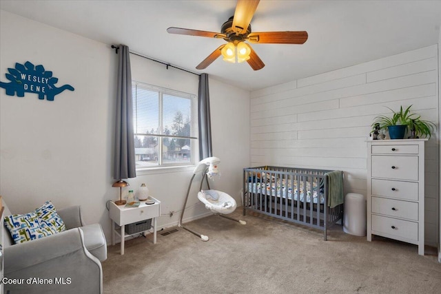 carpeted bedroom featuring a ceiling fan and a nursery area