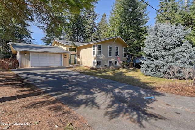 split level home with aphalt driveway, an attached garage, and a front yard