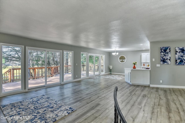 unfurnished living room with light wood finished floors, a notable chandelier, a textured ceiling, and baseboards