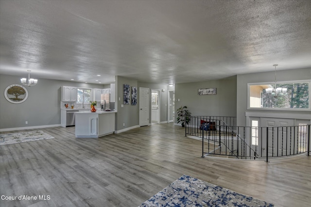 unfurnished living room with a chandelier, light wood finished floors, a textured ceiling, and baseboards