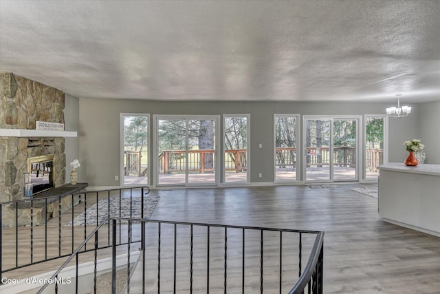 living room featuring a stone fireplace, a healthy amount of sunlight, an inviting chandelier, and wood finished floors