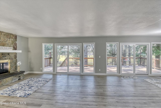 unfurnished living room with baseboards, a textured ceiling, a stone fireplace, and wood finished floors