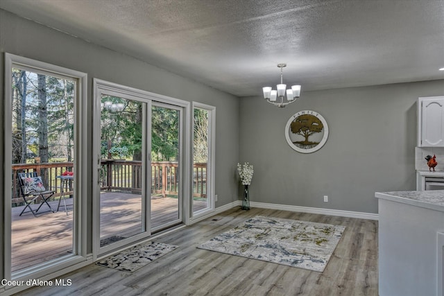 unfurnished dining area featuring a wealth of natural light, a notable chandelier, light wood-type flooring, and baseboards