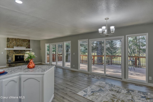 interior space featuring wood finished floors, open floor plan, a stone fireplace, light countertops, and a chandelier