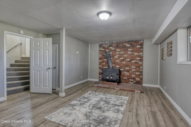 living area with baseboards, stairway, a wood stove, wood finished floors, and a textured ceiling