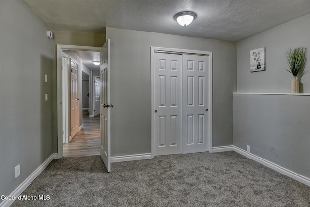 unfurnished bedroom with baseboards, carpet floors, a textured ceiling, and a closet