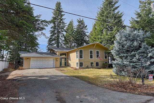 split level home featuring aphalt driveway, fence, a garage, and a front yard