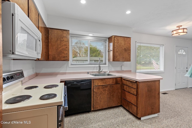 kitchen with a peninsula, white appliances, a sink, light countertops, and brown cabinets