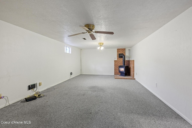 unfurnished living room featuring a textured ceiling, ceiling fan, carpet flooring, baseboards, and a wood stove