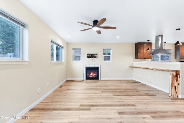 unfurnished living room with light wood-type flooring, a glass covered fireplace, plenty of natural light, and baseboards