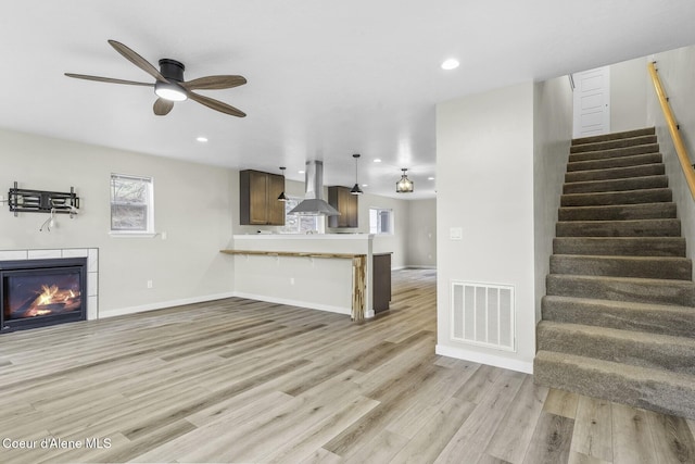 unfurnished living room featuring light wood-style flooring, recessed lighting, visible vents, stairs, and a tiled fireplace