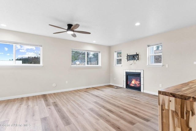 unfurnished living room featuring light wood-style floors, a tile fireplace, and a healthy amount of sunlight